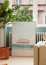 Decoración con cuadros, ideas - Cuadro fotográfico de sombrilla rosa en la playa. Una obra muy veraniega. Elige el tamaño y enmarcación que mejor vaya a tus paredes.