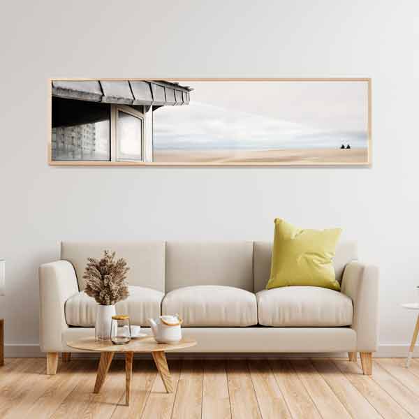 cuadro horizontal encima del sofá y fotográfico de playa con caseta y dos personas mirando el horizonte - kuadro